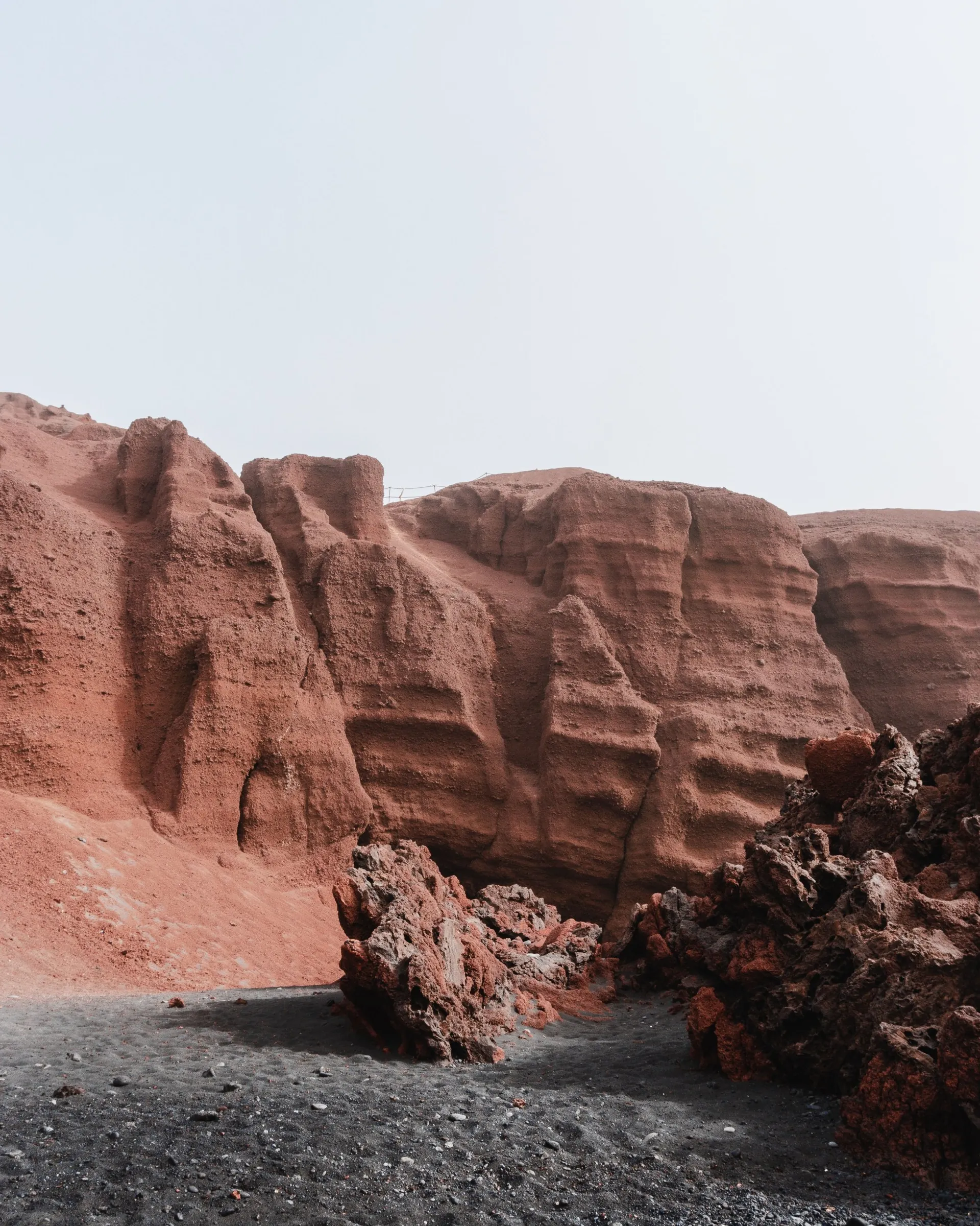 Rust-red volcanic cliffs and dark lava boulders above a black sand beach on Lanzarote