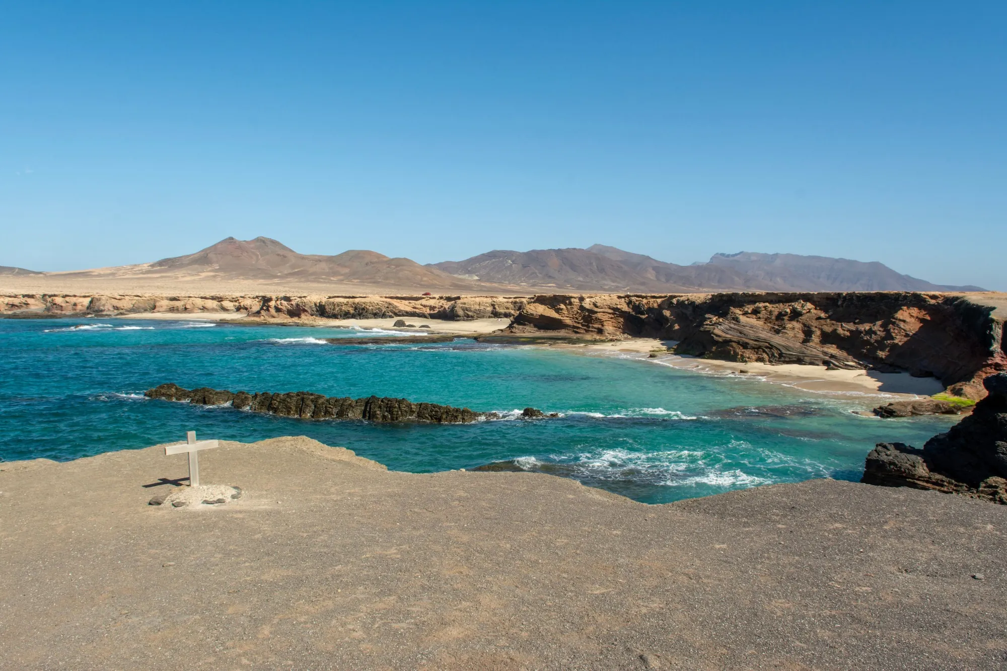 A turquoise bay and sandy coves below pale cliffs, with brown mountains behind