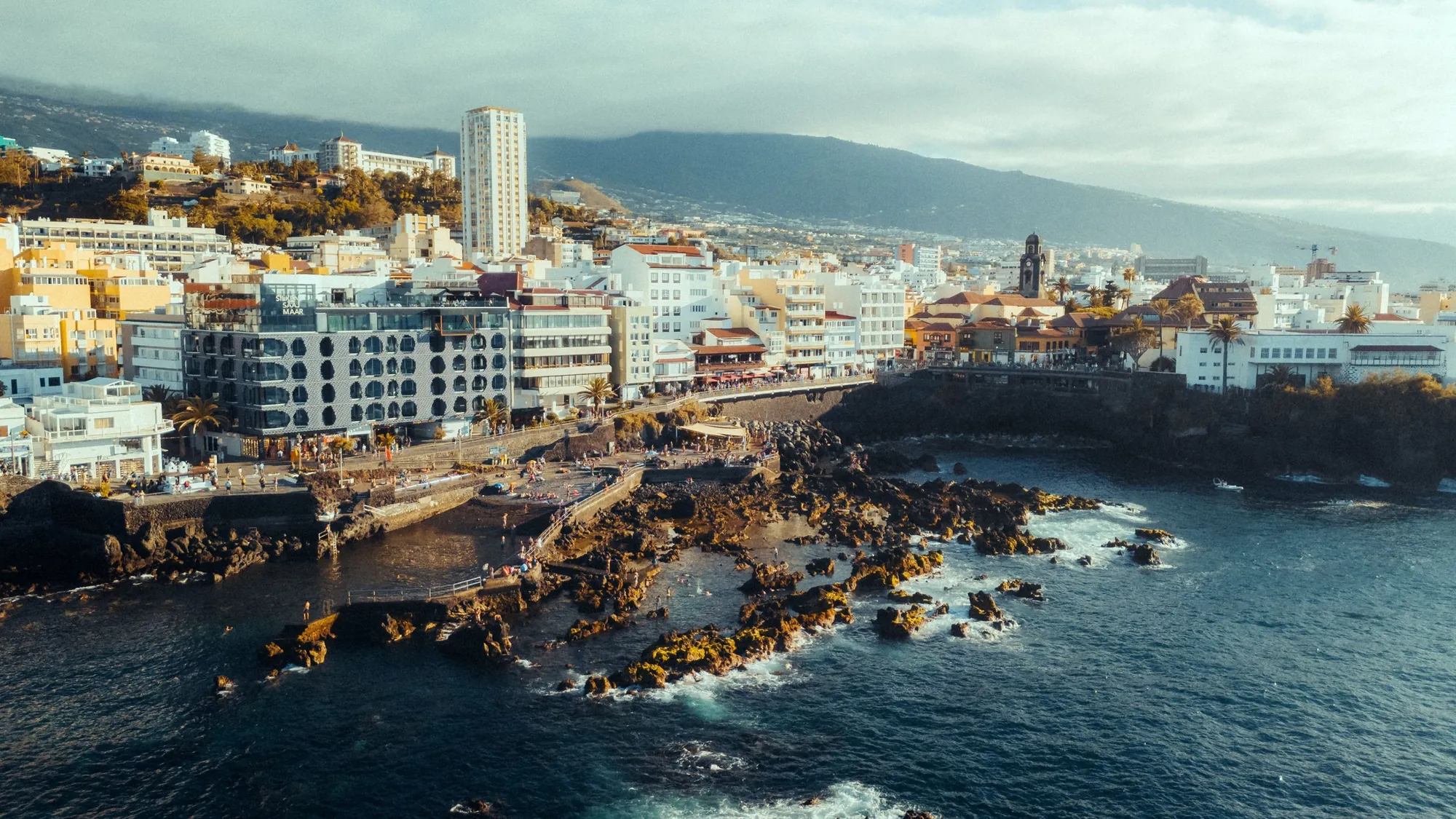 The rocky shore and sea-water pools of Puerto de la Cruz below white and yellow buildings